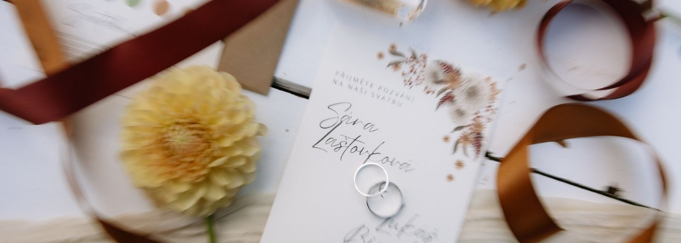svatební flatlay se svatebním oznámením žlutou kytičkou a prstýnky